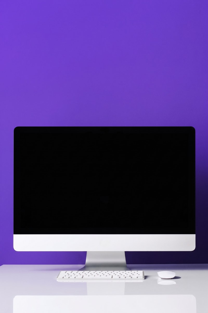 Ordinateur de bureau posé sur un plan de travail, devant un mur violet