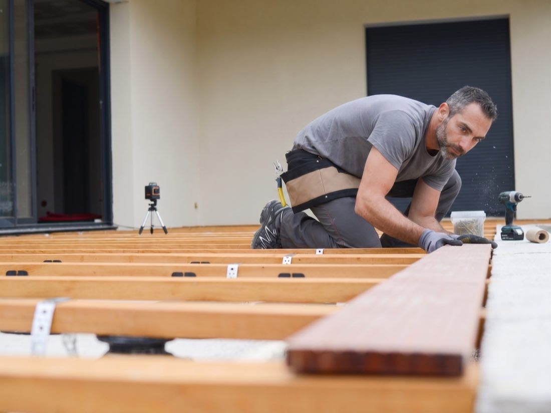 Artisan agenouillé posant les lames d'une terrasse en bois devant une maison